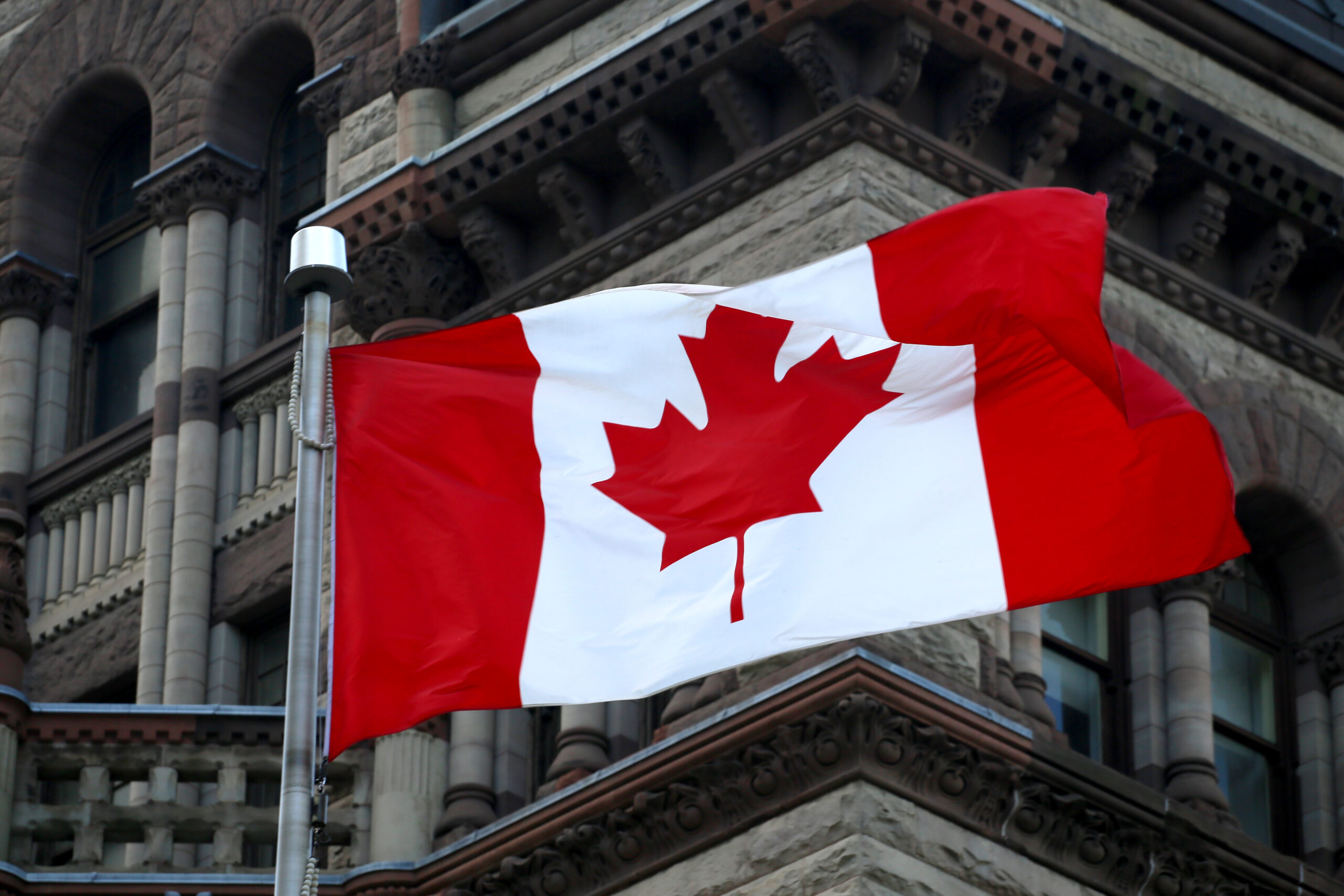 Canadian flag blowing in the breeze in front of a city building.