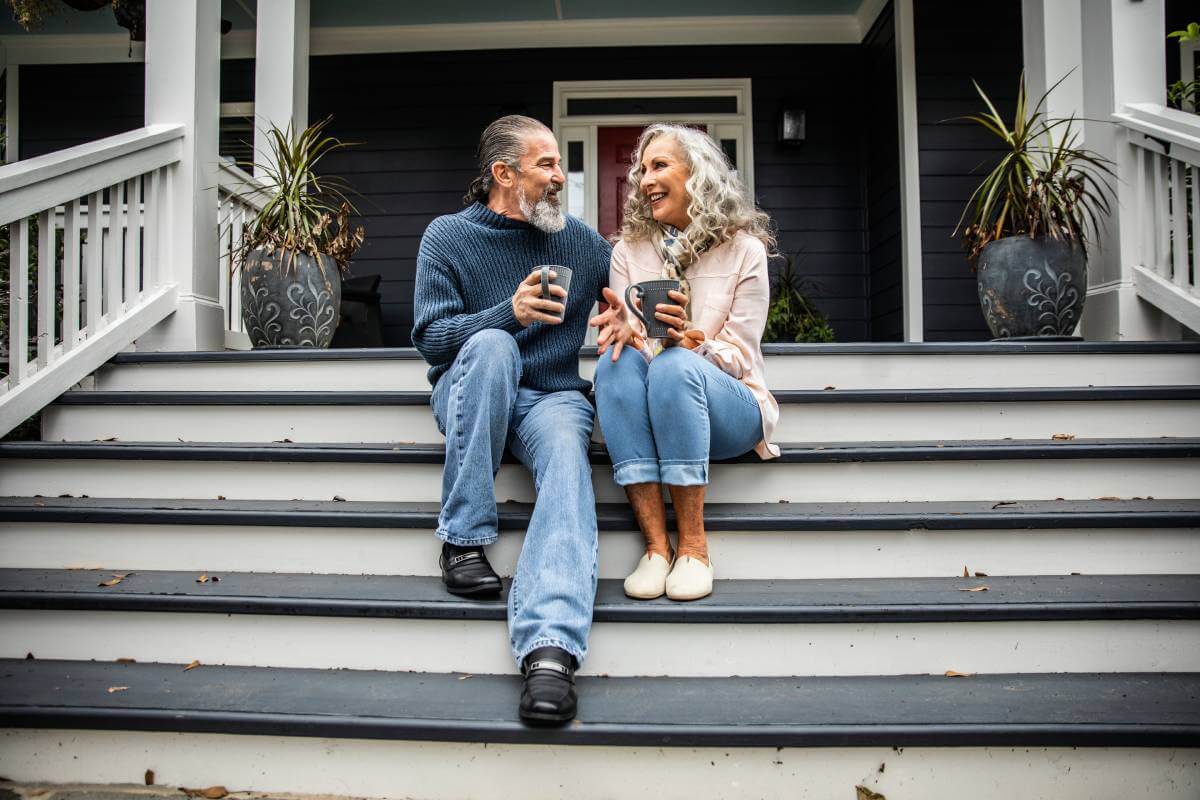 Couple sitting on their porch steps and drinking a beverage.